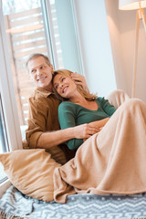 smiling couple hugging while sitting on floor by large window at new home