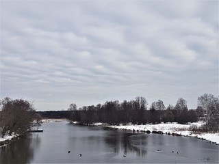 Winter river and snow against a blue sky with clouds.
