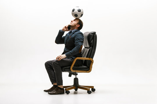 Businessman With Football Ball In Office. Soccer Freestyle. Concept Of Balance And Agility In Business. Manager Perfoming Tricks While Sitting On Chair And Speaking On The Smartphone Isolated On White