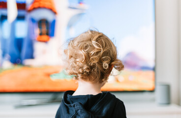 Junges Kind mit blonden Locken vor einem Fernseher