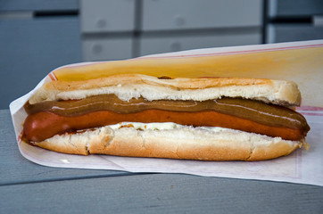 A hot dog, Iceland's national snack, with fried and raw onions, mustard and remoulade, wrapped in waxed paper on a grey wooden table