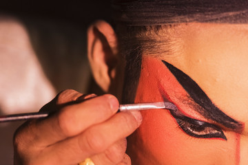 Chinese opera actress is painting her face backstage.
