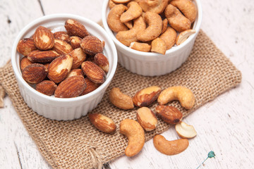 Almonds and cashews in the small cup on the sackcloth and old white woodden background 