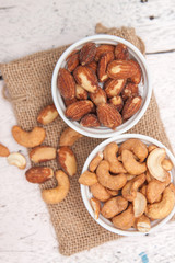 Almonds and cashews in the small cup on the sackcloth and old white woodden background 
