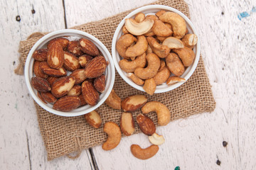 Almonds and cashews in the small cup on the sackcloth and old white woodden background 