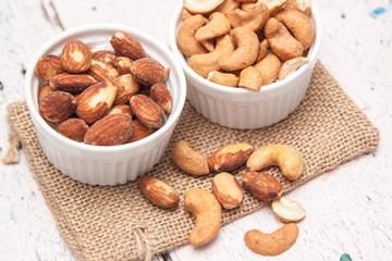 Almonds and cashews in the small cup on the sackcloth and old white woodden background 