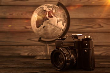 Retro camera, geographical globe on the background of a wooden table. Hobbies, recreation, photography.