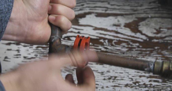 An old copper pipe connection is cut open by male hands using a pipecutter. High angle, static shot.