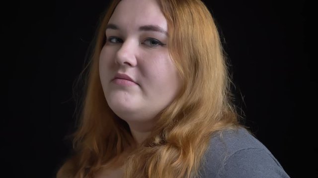 Closeup shoot of young overweight caucasian female turning to camera with background isolated on black