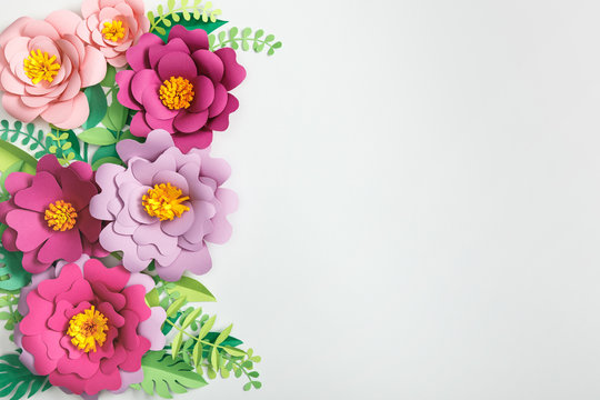 top view of pink and purple paper flowers and green plants with leaves on grey background
