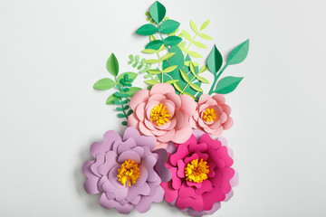 top view of pink and lilac paper flowers with green leaves on grey background