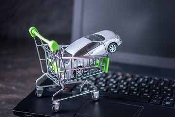 Shopping basket with car on laptop keyboard on dark background. Concept of online shopping vehicles...