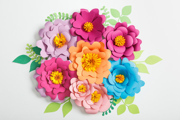 top view of colorful paper flowers and green leaves on grey background