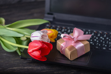 Bouquet of colorful flowers of tulips and a gift box on the laptop keyboard. An unexpected gift for...