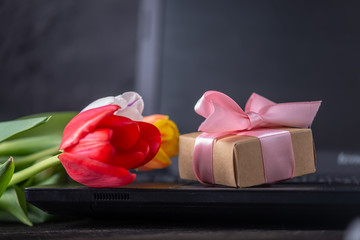 Bouquet of colorful flowers of tulips and a gift box on the laptop keyboard. An unexpected gift for...