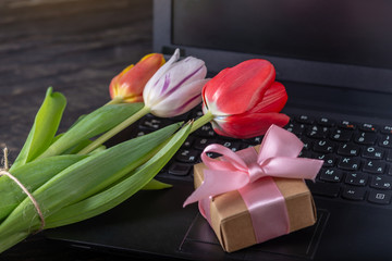 Bouquet of colorful flowers of tulips and a gift box on the laptop keyboard. An unexpected gift for...