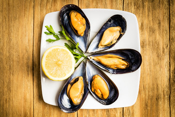 Cooked mussels with parsley and half a lemon on a white plate