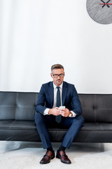 businessman in suit sitting on sofa and holding smartphone