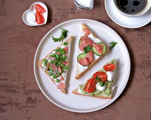 Light breakfast, assorted toasts with a variety of fillings on a white plate. Top view.