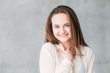 Young woman portrait. Smiling and shy at compliment with hand at neck. Copy space on grey...
