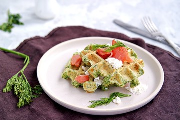Light dinner, lunch or brunch, savory spinach snack waffles with salted salmon and cream cheese on a ceramic plate.