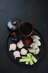 Metal serving tray with steamed hargows and wontons, high angle view on a black stone background
