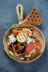 Belgian waffles with trout fillet, grilled zucchini and ricotta cheese in a serving pan, vertical shot on a blue stone surface