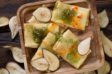 Freshly made crepes topped with sauce and pear fruit chips on a wooden serving tray, view from above