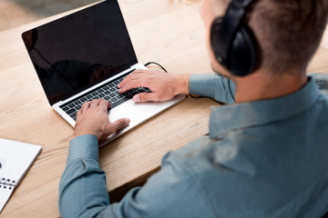 selective focus of man listening music in headphones while using laptop with blank screen