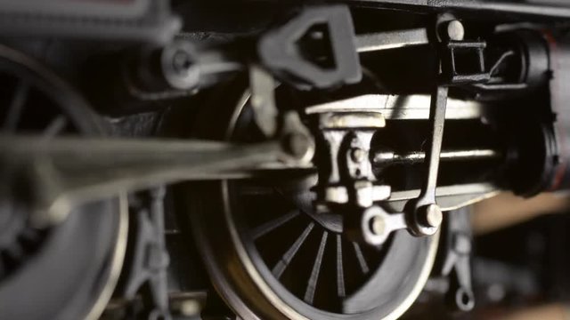 Minature electric powered model steam locomotive driving wheels and connecting rods start turning then accelerate before coming to a stop.