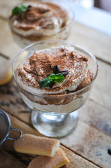 Close-up of classic tiramisu cake in a glass with fresh mint, on wooden background