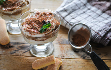 Close-up of classic tiramisu cake in a glass with fresh mint, on wooden background