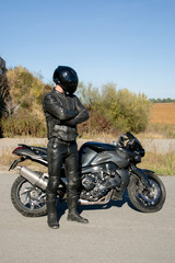 The motorcyclist in black wearing a helmet looks at a motorcycle