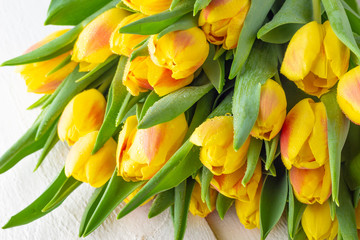 Spring flower yellow red tulips bouquet on white wooden table.