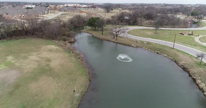 This is an aerial video of Bear Creek Park in Keller Texas.  A water fountain can be seen in the middle of a pond.