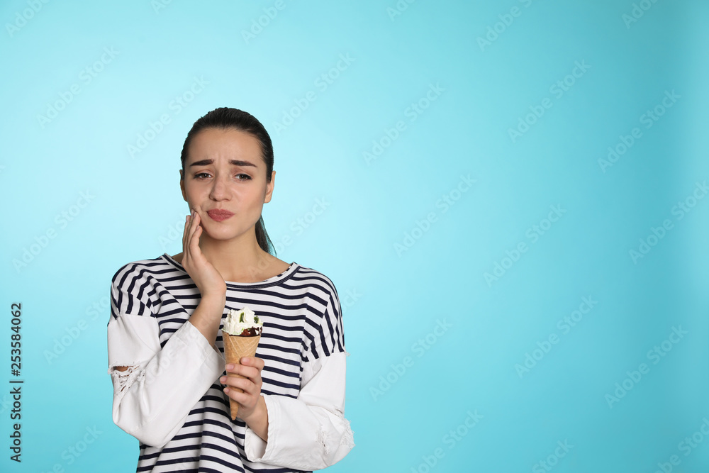 Wall mural emotional young woman with sensitive teeth and ice cream on color background. space for text