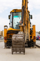 Excavator bucket rests on the asphalt. Yellow excavator with a lowered bucket on a city street on a...