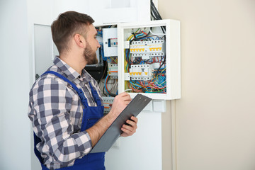 Male electrician with clipboard near fuse board indoors, space for text