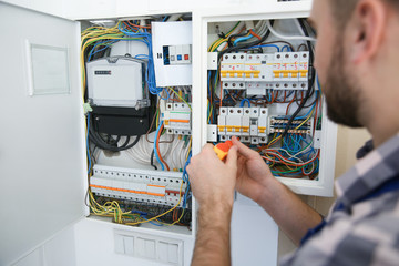 Electrician repairing fuse box with screwdriver indoors, closeup