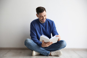 Handsome man reading book on floor near wall