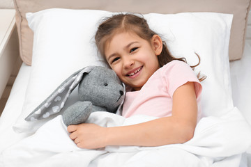 Cute child with stuffed rabbit resting in bed at hospital