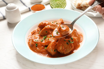 Woman eating tasty butter chicken at table, closeup. Traditional Murgh Makhani dish