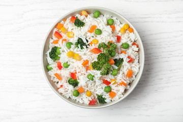 Bowl with tasty rice and vegetables on wooden background, top view