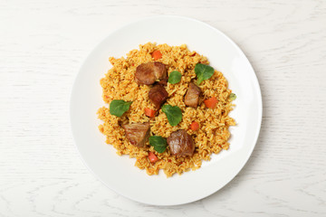 Plate with delicious rice pilaf on wooden background, top view