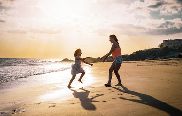 Fototapeta na wymiar Mother and daughter playing on the beach at sunset - Happy family having fun in vacation on the beach - Parenthood, happiness and love concept