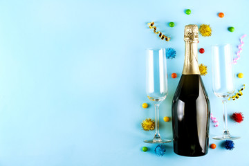 Bottle of champagne, pair of flute glasses with confetti, streamers and other party attributes in flat lay composition on pale blue paper background. Close up, copy space, top view.