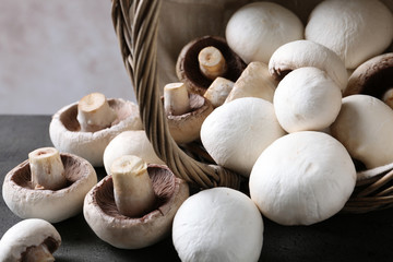 Fresh champignon mushrooms scattered from basket on table, closeup