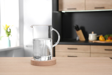 Glass jug with water on wooden table in kitchen