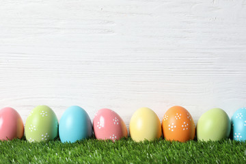 Colorful painted Easter eggs on green grass against wooden background, space for text