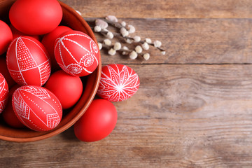 Bowl with red painted Easter eggs on wooden background, top view. Space for text